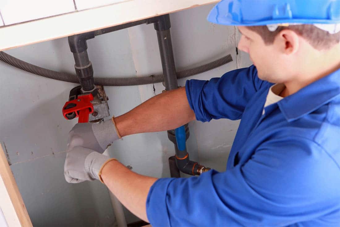 plumbing-LeakDetectionAndRepair-Supporting-1100×734 Plumber using a wrench to fix a leaky pipe under a sink